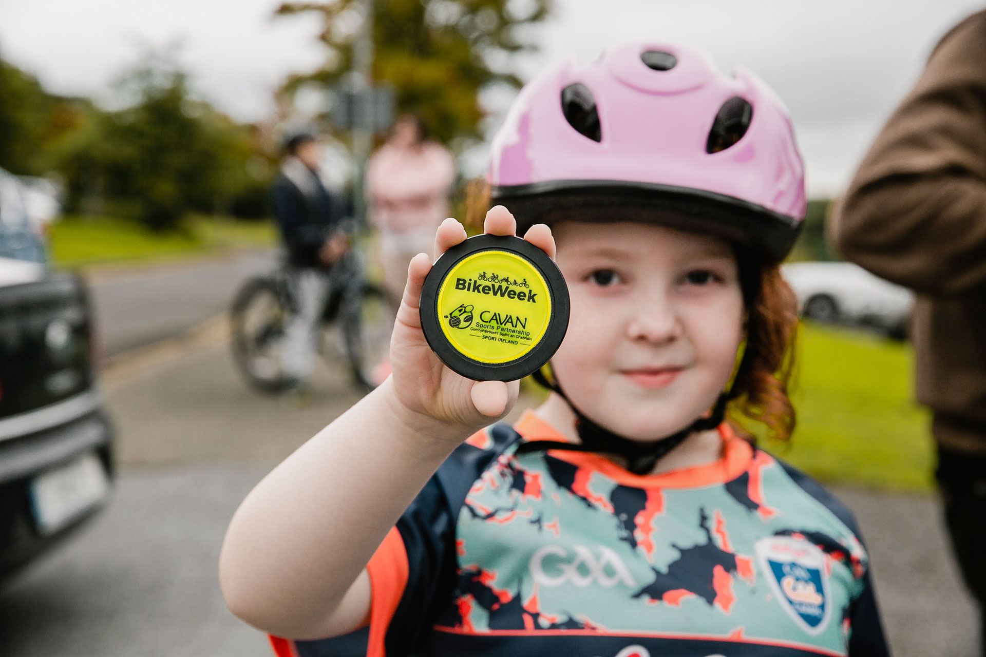 Young girl with bike helmet on holding yellow Bike Week sign.