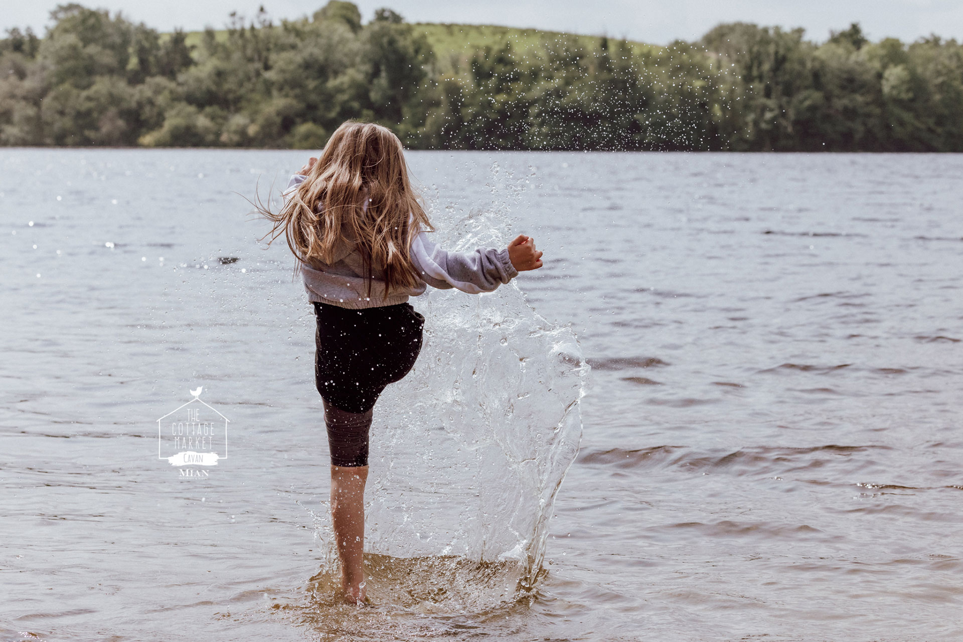 Young girl with back turned kicking water in air.