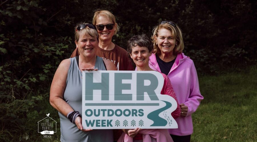 Four women hold sign for HER Outdoors week.