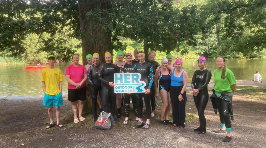 Group of women and a male lifeguard hold sign for HER Outdoors week.
