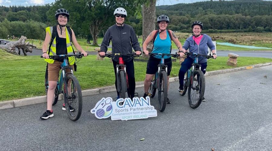 Four people smile while sitting on bikes.