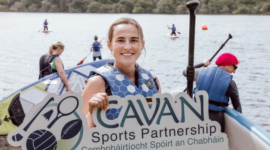 Women smiles in front of lake where women are paddle boarding.