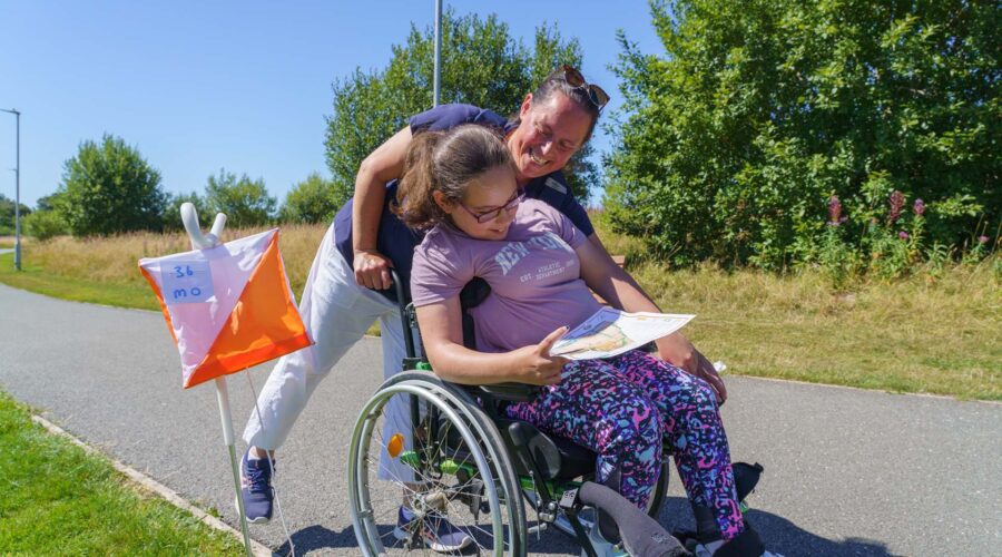 Women pushes girl in wheelchair on a sunny day.