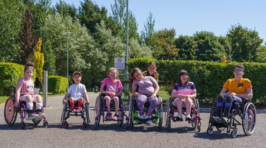 Group of children in wheelchairs smile on a sunny day.